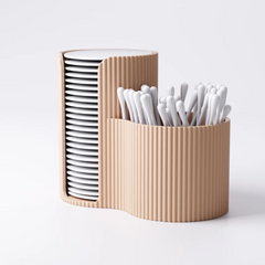 A beige, fluted cotton pad and bud holder on a white background, filled with cotton pads and swabs.
Top-down view of the ribbed bathroom organiser showing the two curved compartments.
A modern, ribbed makeup tidy in a light pink colour, sitting on a marble bathroom counter.