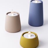 Ridged tealight holder shown in three sizes and colours — mustard yellow, beige, and royal blue, each with a flameless LED tealight lit