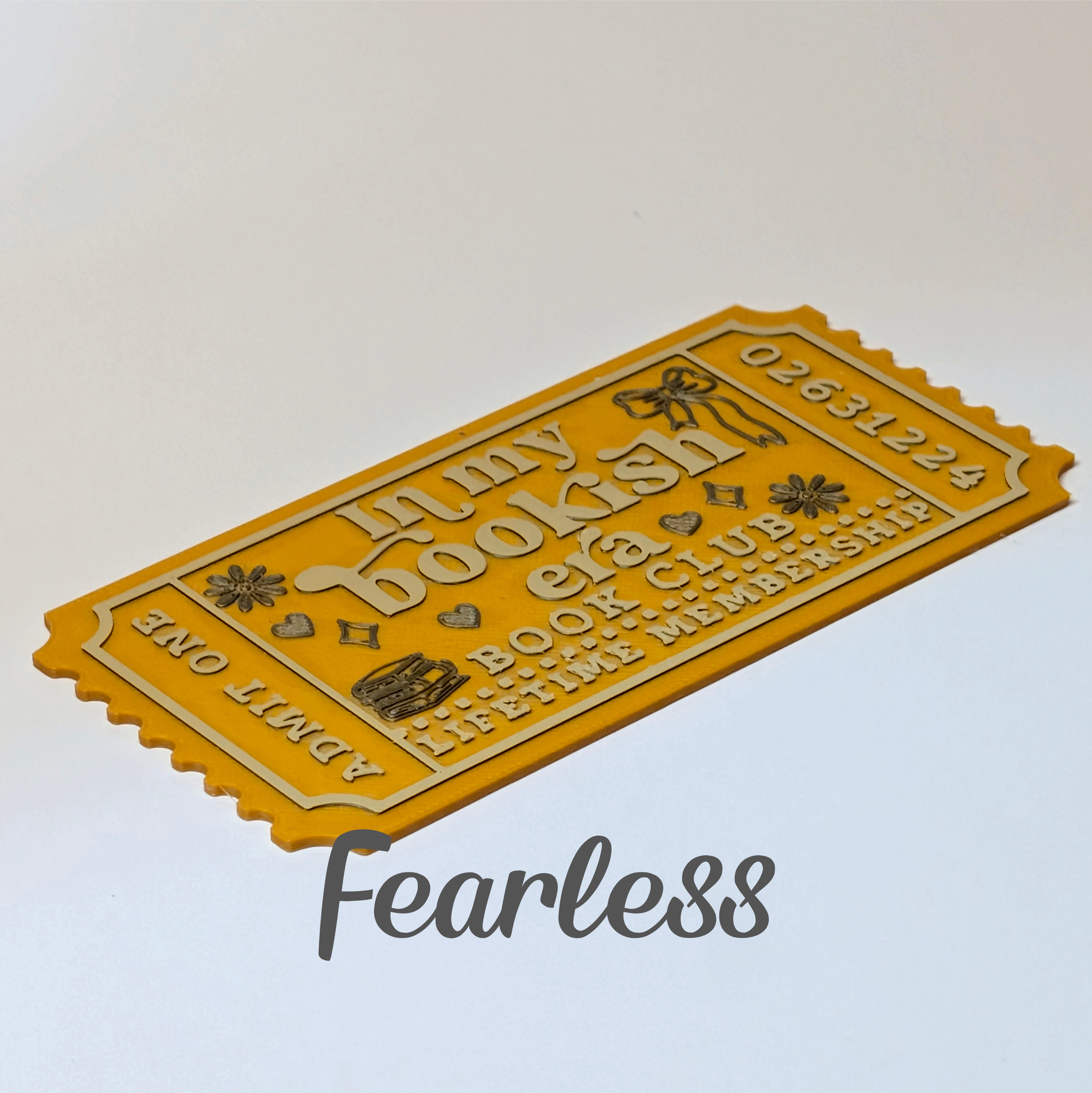 A yellow novelty ticket-shaped item with embossed text reading 'Lunzy Bookish' and 'Book Club Lifetime Membership,' shown on a plain light background with a large 'Fearless' watermark below.