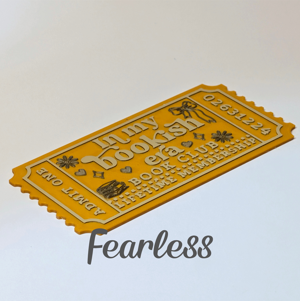 A yellow novelty ticket-shaped item with embossed text reading 'Lunzy Bookish' and 'Book Club Lifetime Membership,' shown on a plain light background with a large 'Fearless' watermark below.
