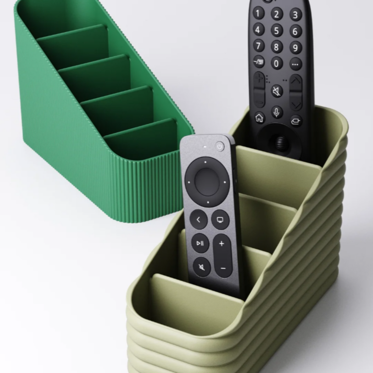 A Modern, olive green and grass green remote control holders. one with a 'Vertical Narrow-Ribbed' texture, and the other a 'horizonal wide fluted design, both sitting on a white background.
A white remote caddy with a 'Horizontal Wide-Fluted' texture, showing the bold, stacked lines.
Side view of the 5-slot tiered remote caddy, showing the 'stadium seating' design that holds remotes at an angle.
A black remote organiser on a wooden coffee table, holding three TV remotes and a pair of glasses.