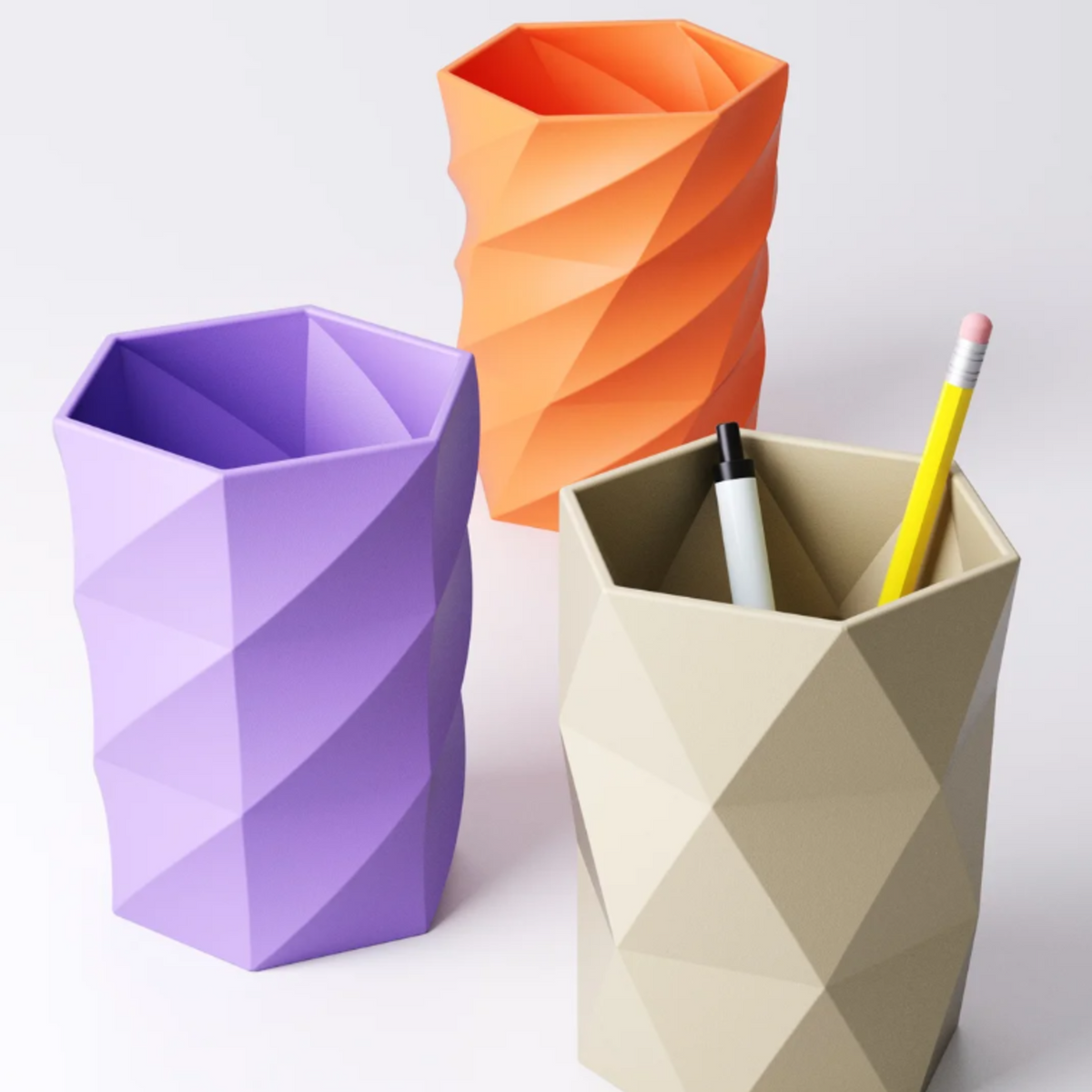 Three geometric pen pots in purple, orange, and beige, shown on a white background.
A beige faceted pen pot holding a pencil and a marker.
A purple pen pot with a 'Wide Twist' design, next to an orange pot with a 'Narrow Twist' design.