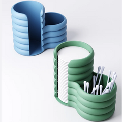 A modern, green cotton pad and bud holder with a 'Wide Fluted' or wavy texture, filled with cotton pads and swabs.
Side view of the bubbly bathroom organiser showing the cotton pad dispenser slot.
A white, wavy-textured makeup tidy on a marble vanity counter, next to a perfume bottle.