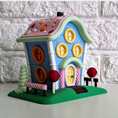 whimsical 3D printed candy fairy house in bright blue, pink, and yellow, with a candy-dot roof and lollipop decorations, shown on a table.
A cute, colourful light-up fairy house, shown from the front against a white brick wall.
Close-up of the candy-themed details on a 3D printed fairy house, including lollipop trees and a sweet-covered roof.