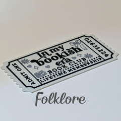 A white paper-style ticket with black decorative text reading 'In my bookish era BOOK CLUB LIFETIME MEMBERSHIP' and 'ADMIT ONE,' photographed on a light neutral background. A gray 'Folklore' watermark appears below the ticket.