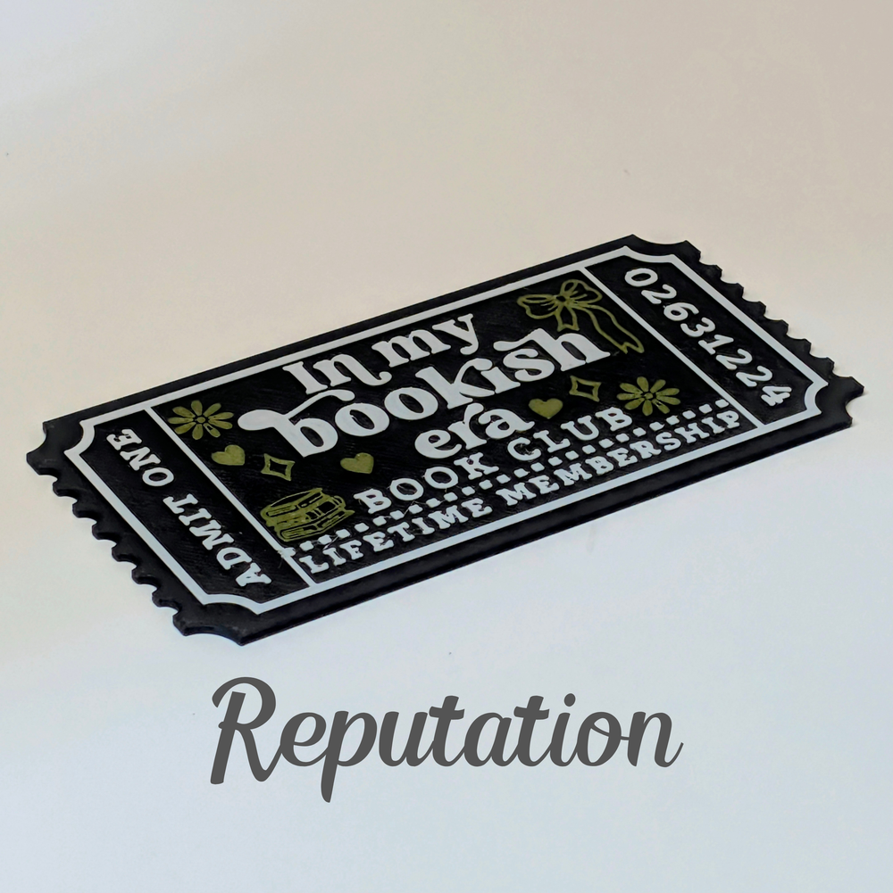 A black and white book-themed membership ticket with gold decorative accents, displayed on a light beige background with the word 'Reputation' written below.