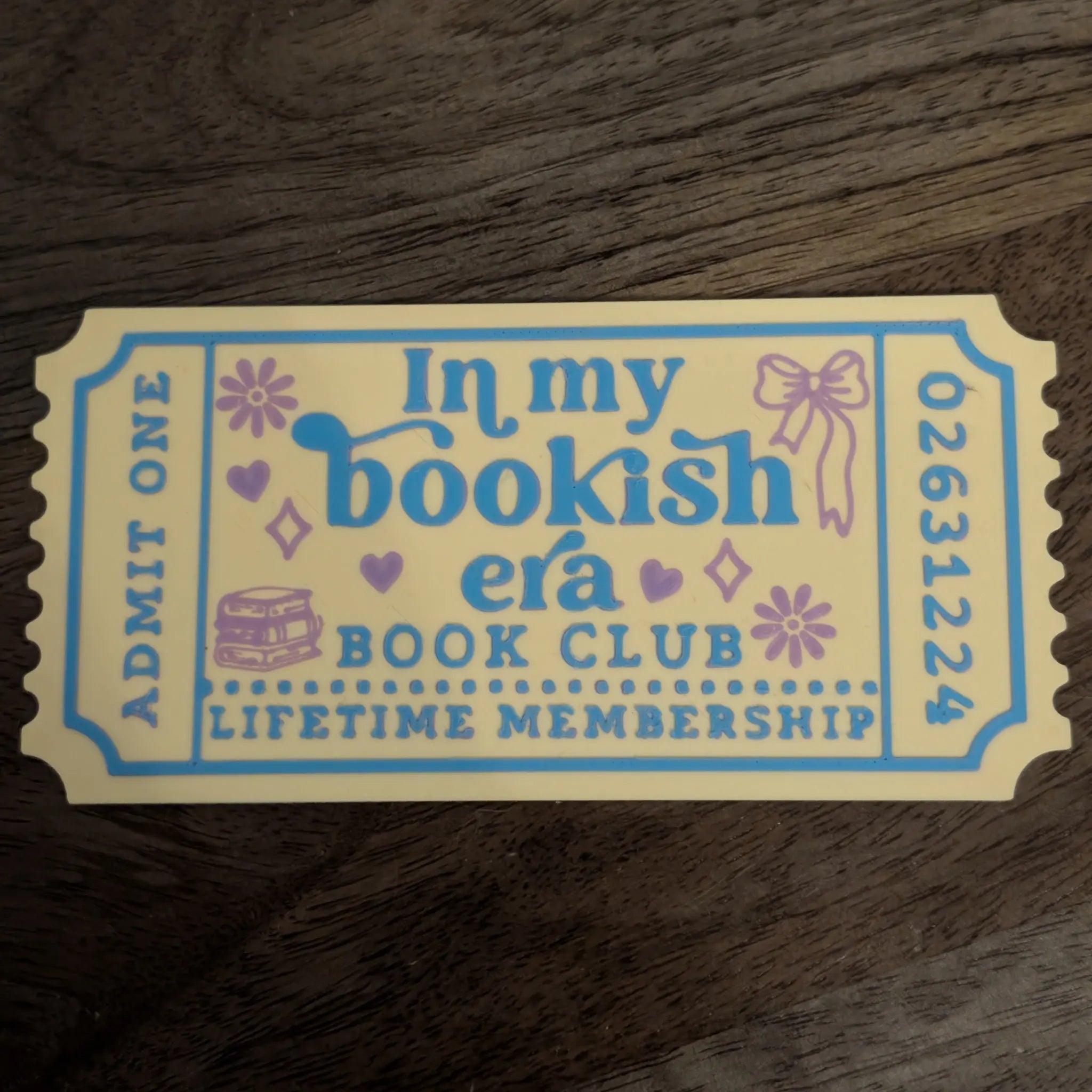 In My Bookish Era ticket bookmark photographed on hardback novels with cream and yellow design