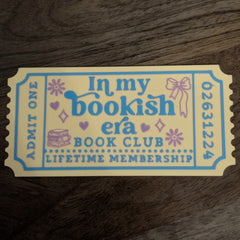 In My Bookish Era ticket bookmark photographed on hardback novels with cream and yellow design